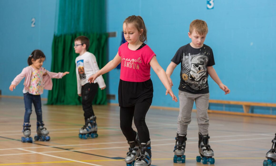 four children roller skating in a sports hall